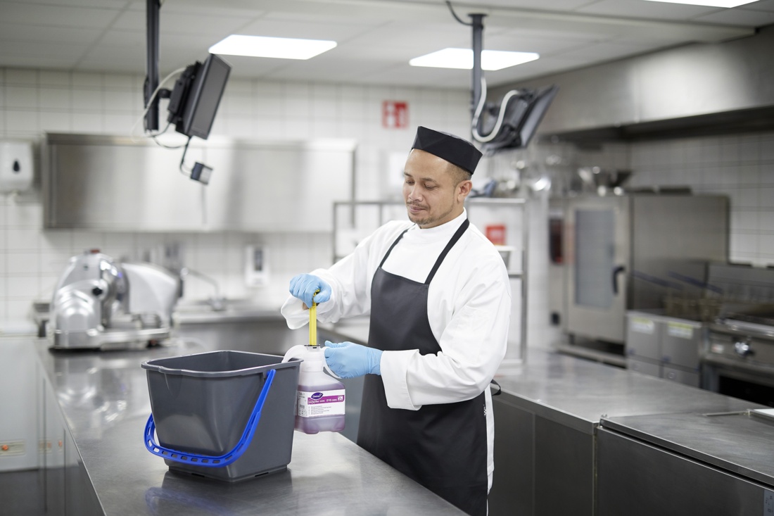 Mitarbeiter in Gastro-Küche mit Reinigungsmittel